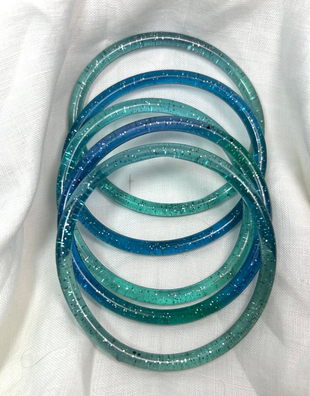 Four teal and blue glitter jelly bangle bracelets stacked together